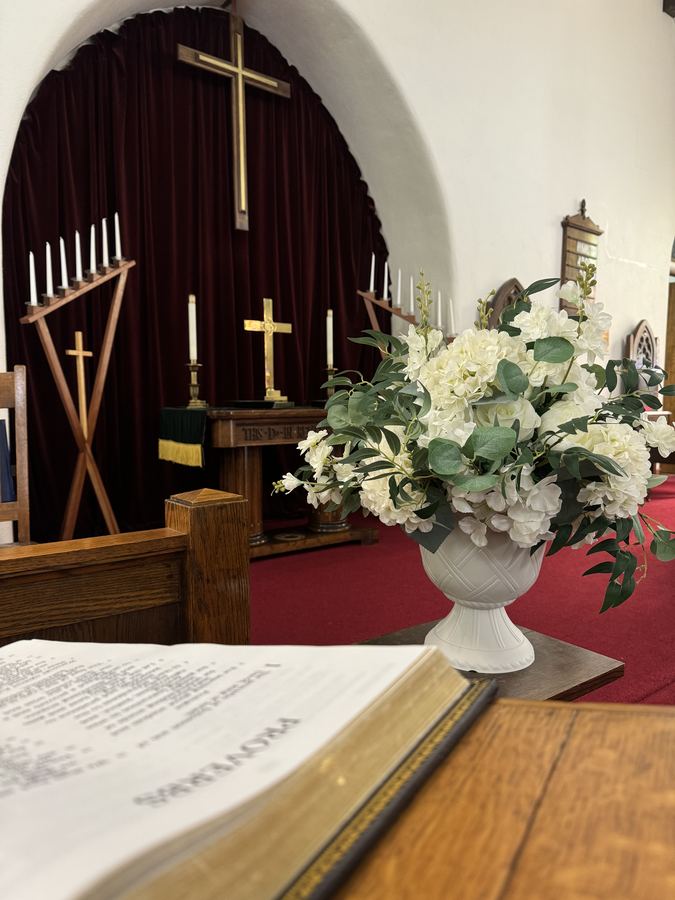The sanctuary of First Congregational Church — open Bible, white floral arrangement, brass cross and deep red velvet drapery
